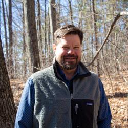 Man in blue shirt and grey zip up vest.
