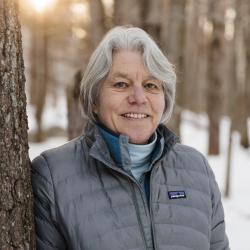 Susan Arnold poses outside in winter next to a tree.