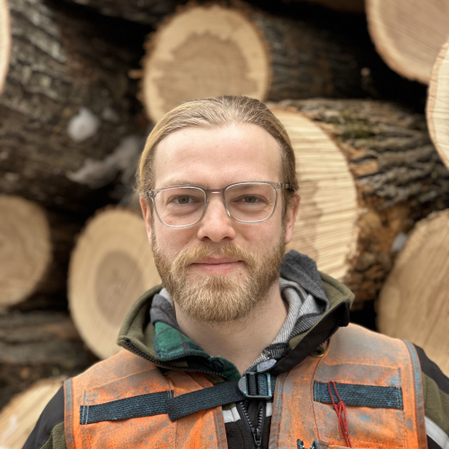 Ben poses in front of a pile of timber harvested.