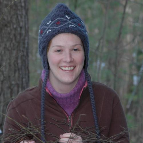 Ann McCoy poses in a winter hat in a snow-covered forest.