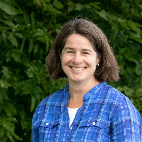 Anne Truslow poses in front of green leaves near the Conservation Center.