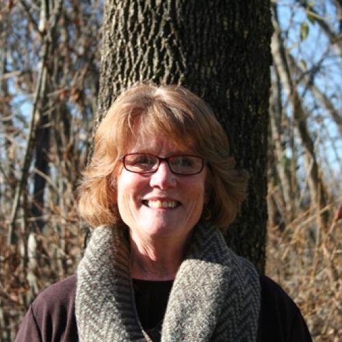 Rita Carroll poses against the trunk of a tree.