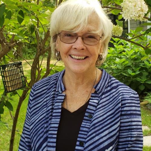 Deb Buxton poses for a photo outside among blooming shrubs.