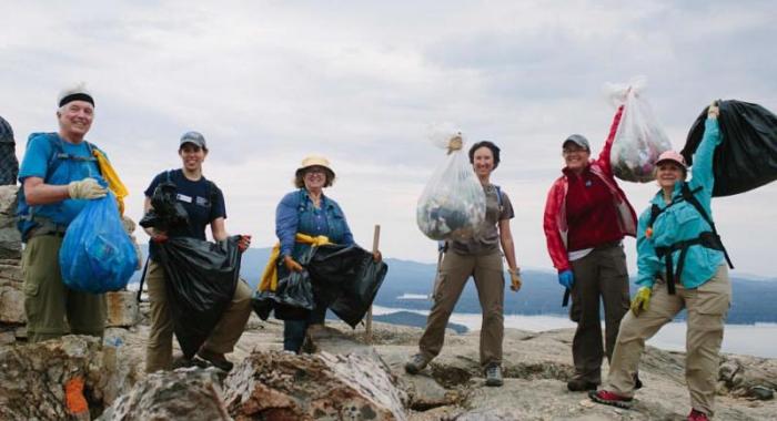 A group of individuals holding full trash bags at the summit of a mountain on a grey sky day.