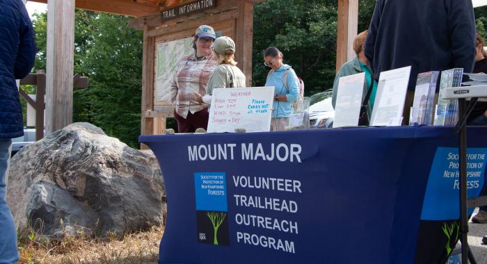 A blue table cloth reads "Mt Major Volunteer Trailhead Outreach Program"
