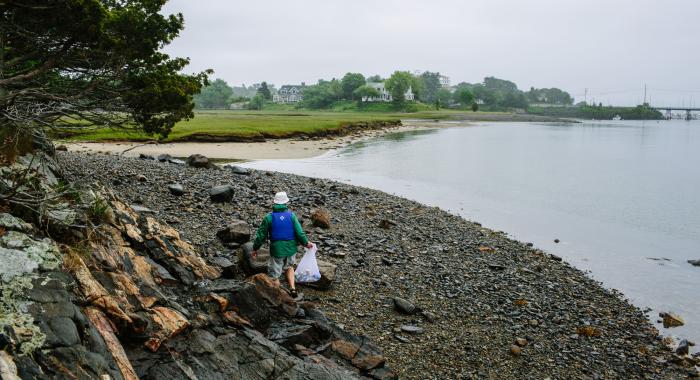 Young boy walks down a beach holding a plastic bag