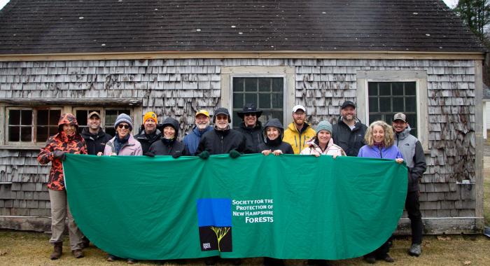 land steward class of 2025 holding banner in front of cedar shake building