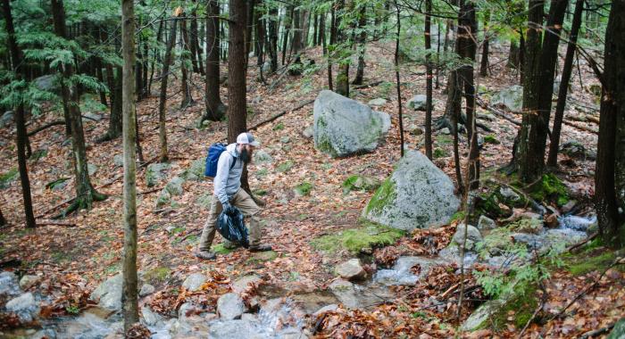a lone hiker on trail in dense forest area with a black trash bag.