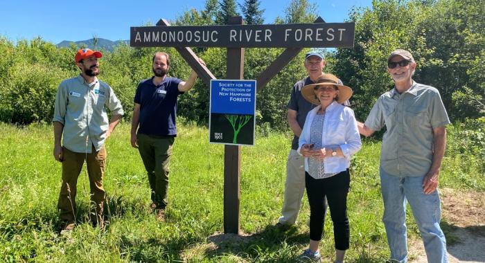 A group of staff and community members pose at the entrance to the Ammonoosuc River Forest.