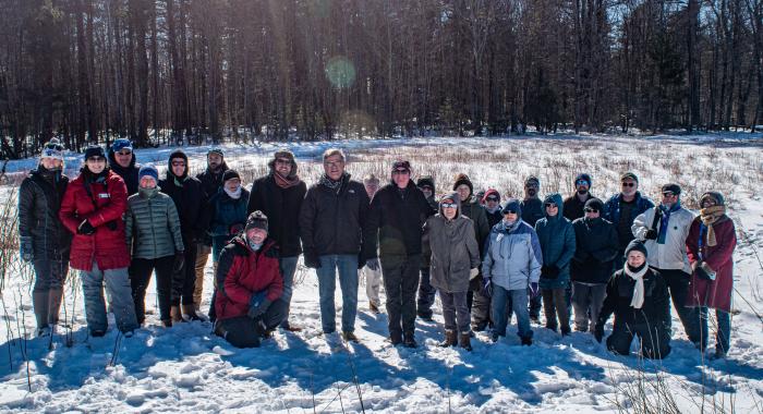 A group gathers in front of a snowy forest for a photo commemorating the expansion of Champlin Forest.