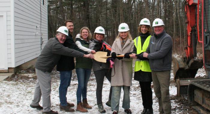 A group of community and business leaders holds a golden shovel together at the groundbreaking site.