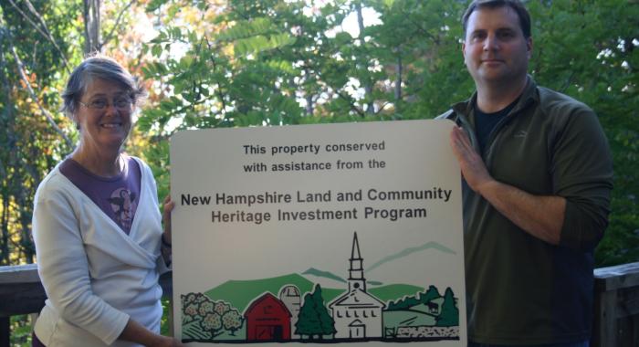 Dijit Taylor, Executive Director of LCHIP Standing next to Brian Hotz VP of Land Conservation holding a LCHIP sign between them