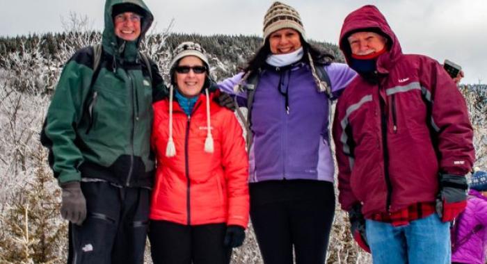 A group of four hikers stands at the top of a snowy viewpoint on Mount Monadnock.