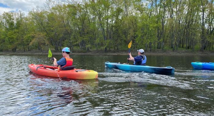 A father and son, both in lifejackets, kayak together on the Merrimack River.