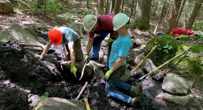 A group huddles around a muddy hole.
