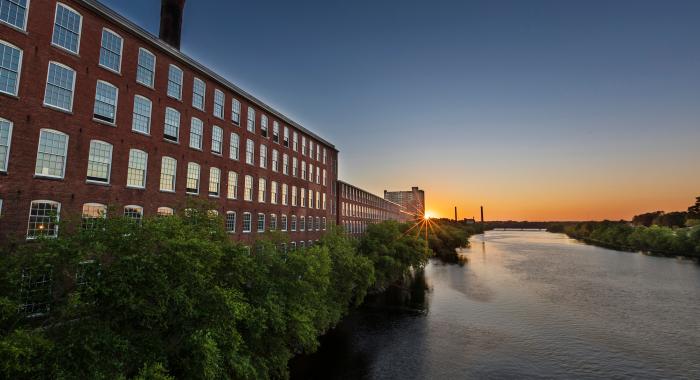 A river at sunset winds past a former mill building in Lowell.