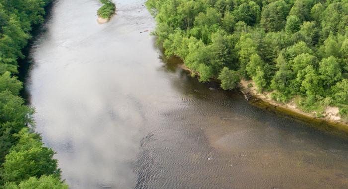 A view from above of a bend in the Merrimack River, lined with green forests.