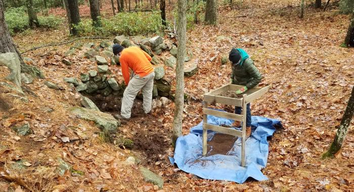 Two archaeologists look down into a cellar hole at Monson Center.