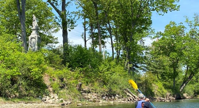 Dave Anderson paddles by a statue and looks up from the river.