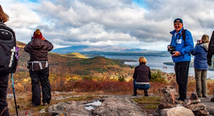 Hikers enjoying autumn view of Lake Winnipesaukee and Belknap Range from summit of Pine Mountain on Forest Society Morse Preserve