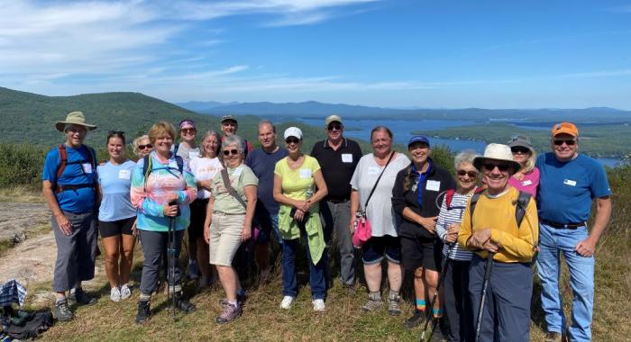 colorful hikers pose at open summit for portrait with scenic mountains and lake background