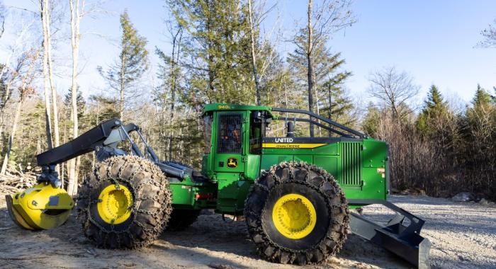 A green grapple skidder parked on log landing at active winter timber harvest