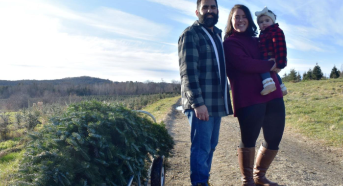 A couple poses with their infant and their fresh-cut Christmas tree at The Rocks.