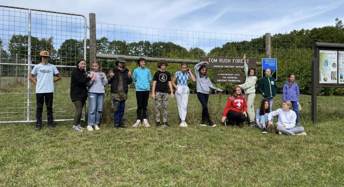 7th graders from The Well School pose in front of the chestnut orchard sign at Tom Rush Forest.