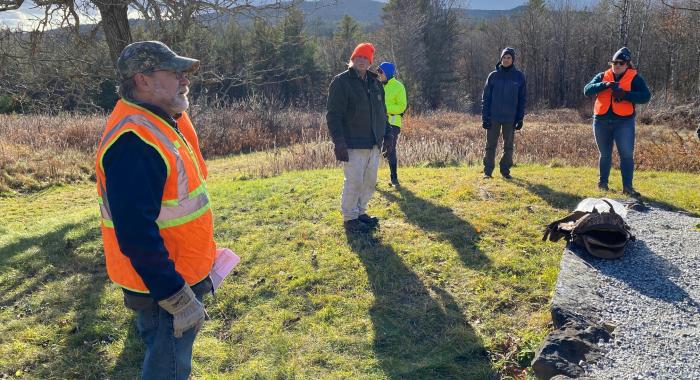 Staff in orange hats and vests view the new marker on a large granite stone at the forest.