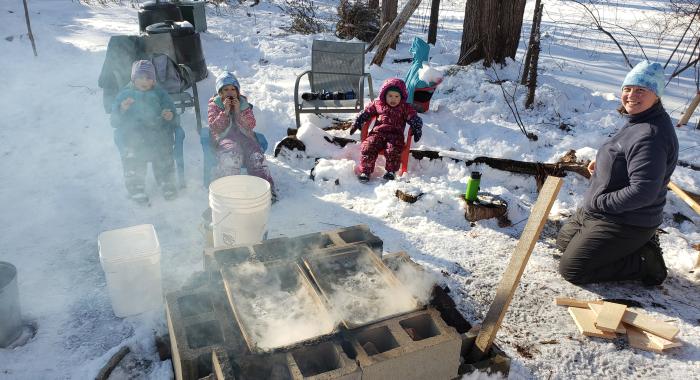 Gabe Roxby and his three daughters and wife sit outside around a fire while boiling sap.