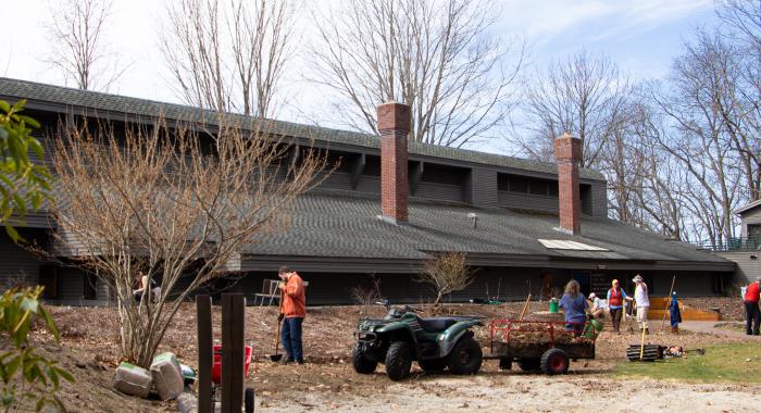 A group of workers hold rakes and stand next to wheel barrows in front of a grey building 