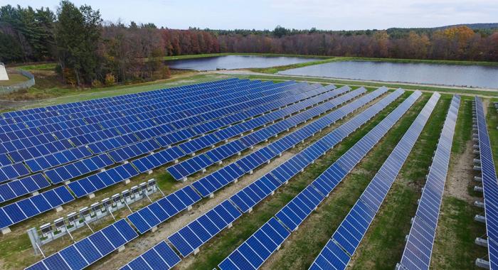 three large fields of solar panels surrounded by forest