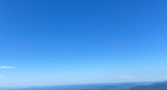 Woman sits on the edge of a large rock at the top of a mountain looking out to the view 