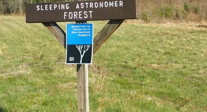 The Forest Society sign at the Sleeping Astronomer forest, with the rock formation in the far background.
