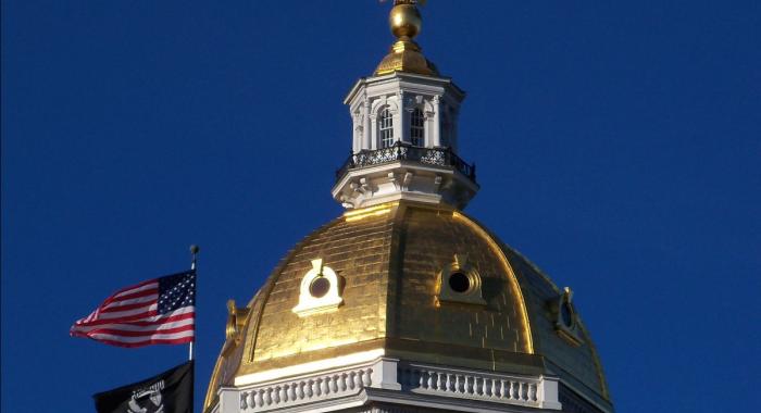 NH State Capital Dome against blue sky, American and POW flag waving