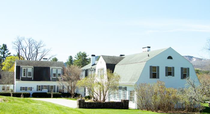 White house with green shutters on a green lawn in front of a small ski mountain 