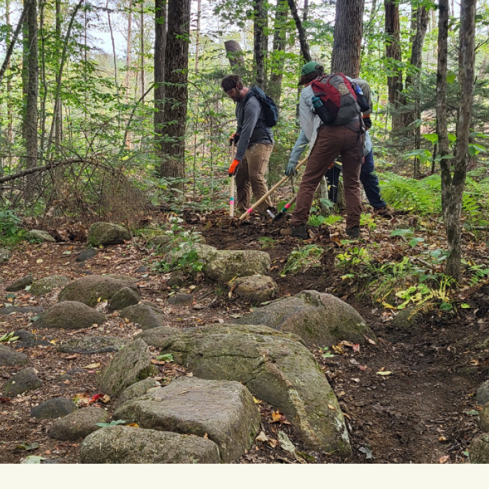 3 people with tools on a trail moving sediment from drainage feature.
