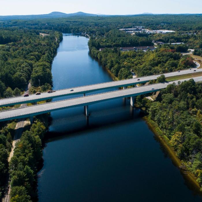 A river runs underneath interstate 93 with mountains in the background.