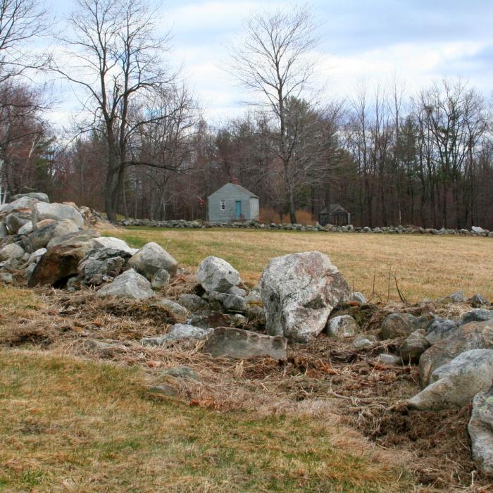 A stone wall at Monson Center with the historic home in the background.