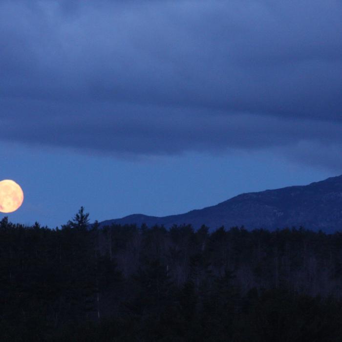 A moon rises over the mountain.