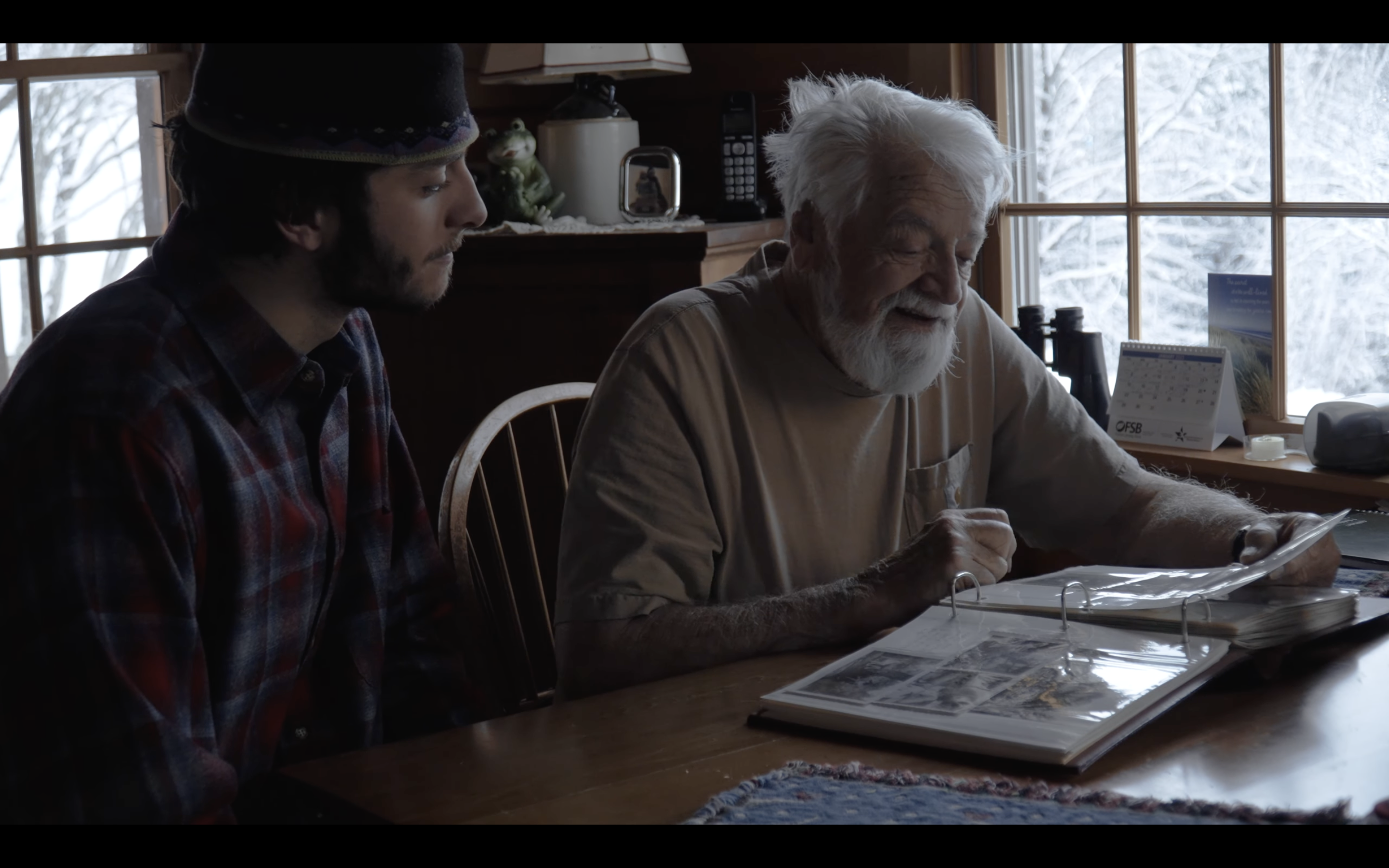 Older man and grandson look at a book at a table.