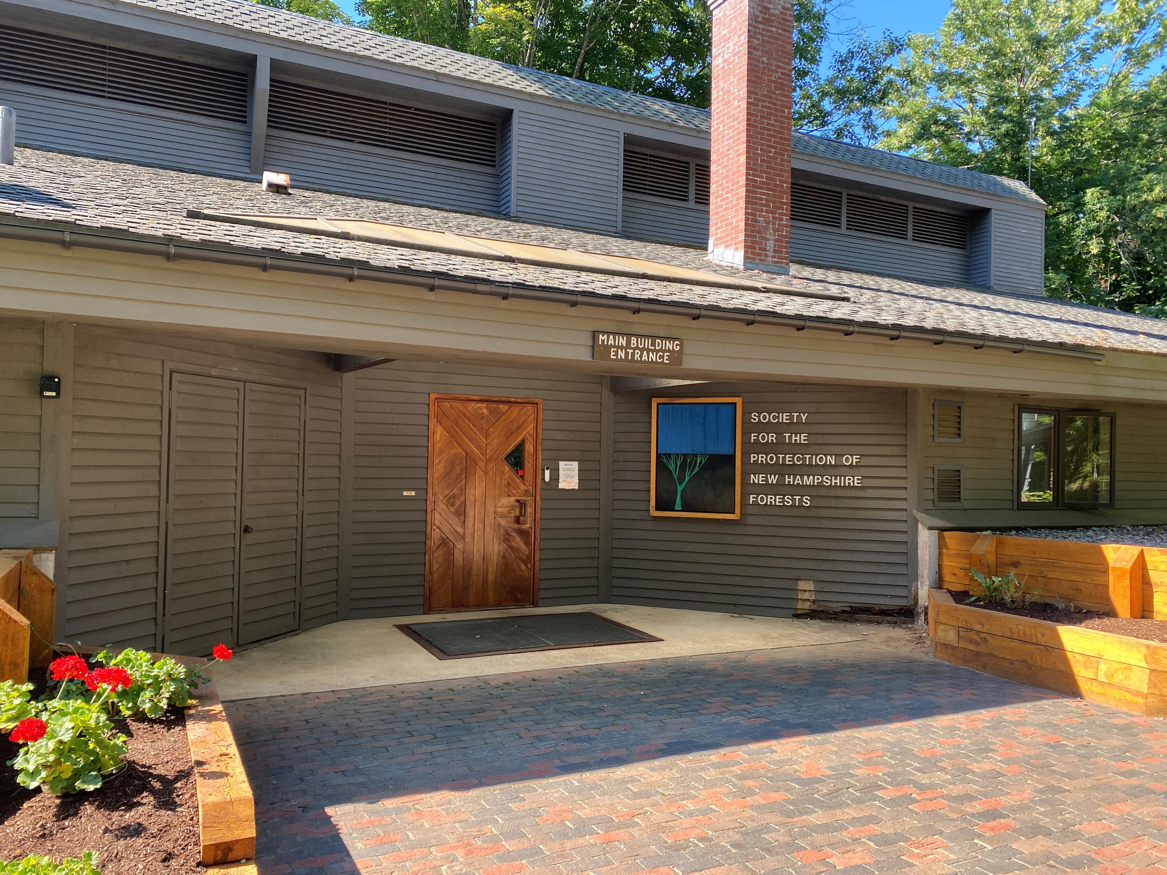 A large grey building with a wooden front door and a blue and green sign