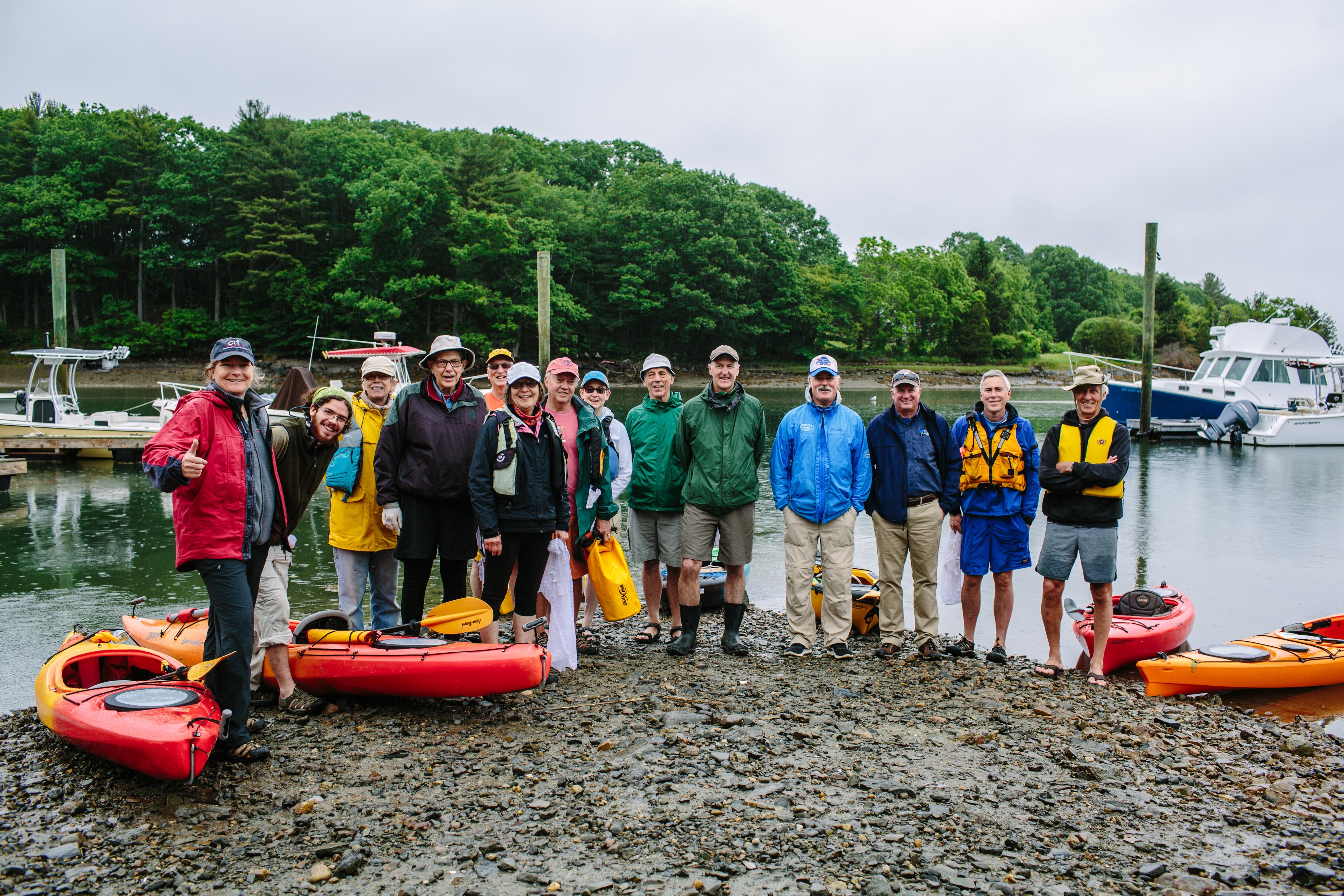 A group of people in raincoats stand on a beach with kayaks