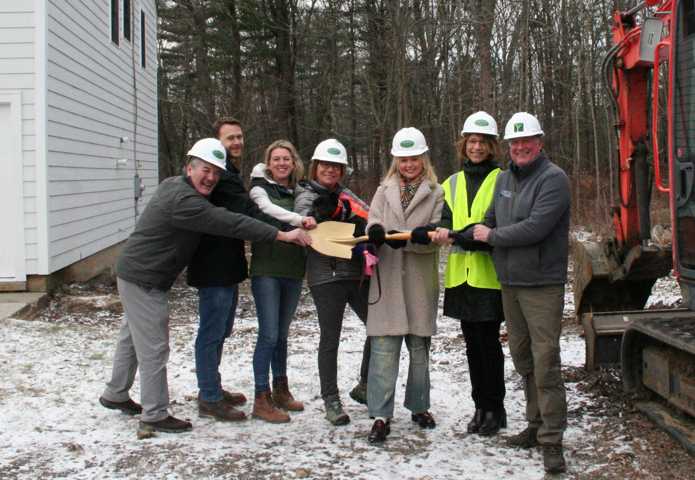 A group of community and business leaders holds a golden shovel together at the groundbreaking site.