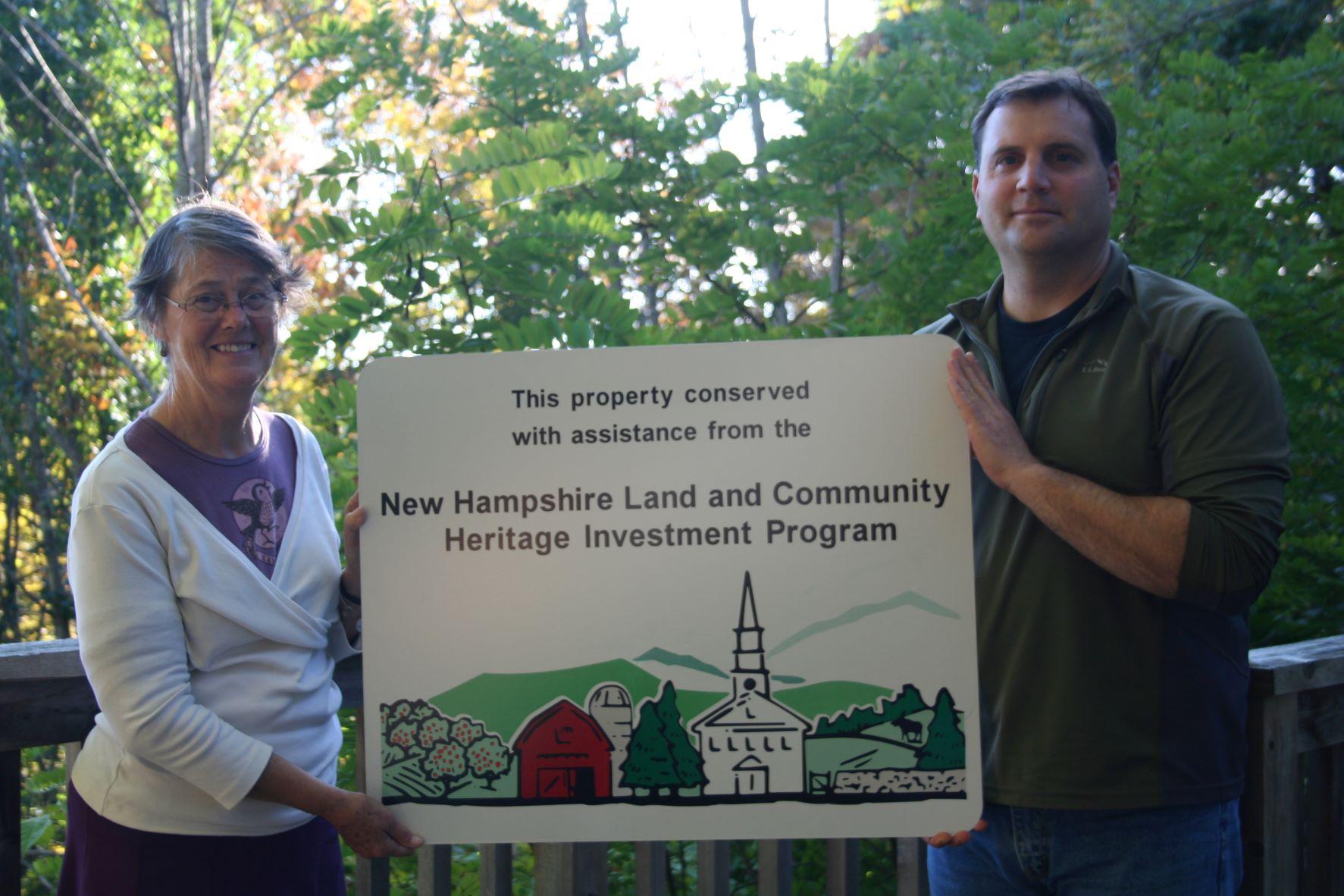 Dijit Taylor, Executive Director of LCHIP Standing next to Brian Hotz VP of Land Conservation holding a LCHIP sign between them