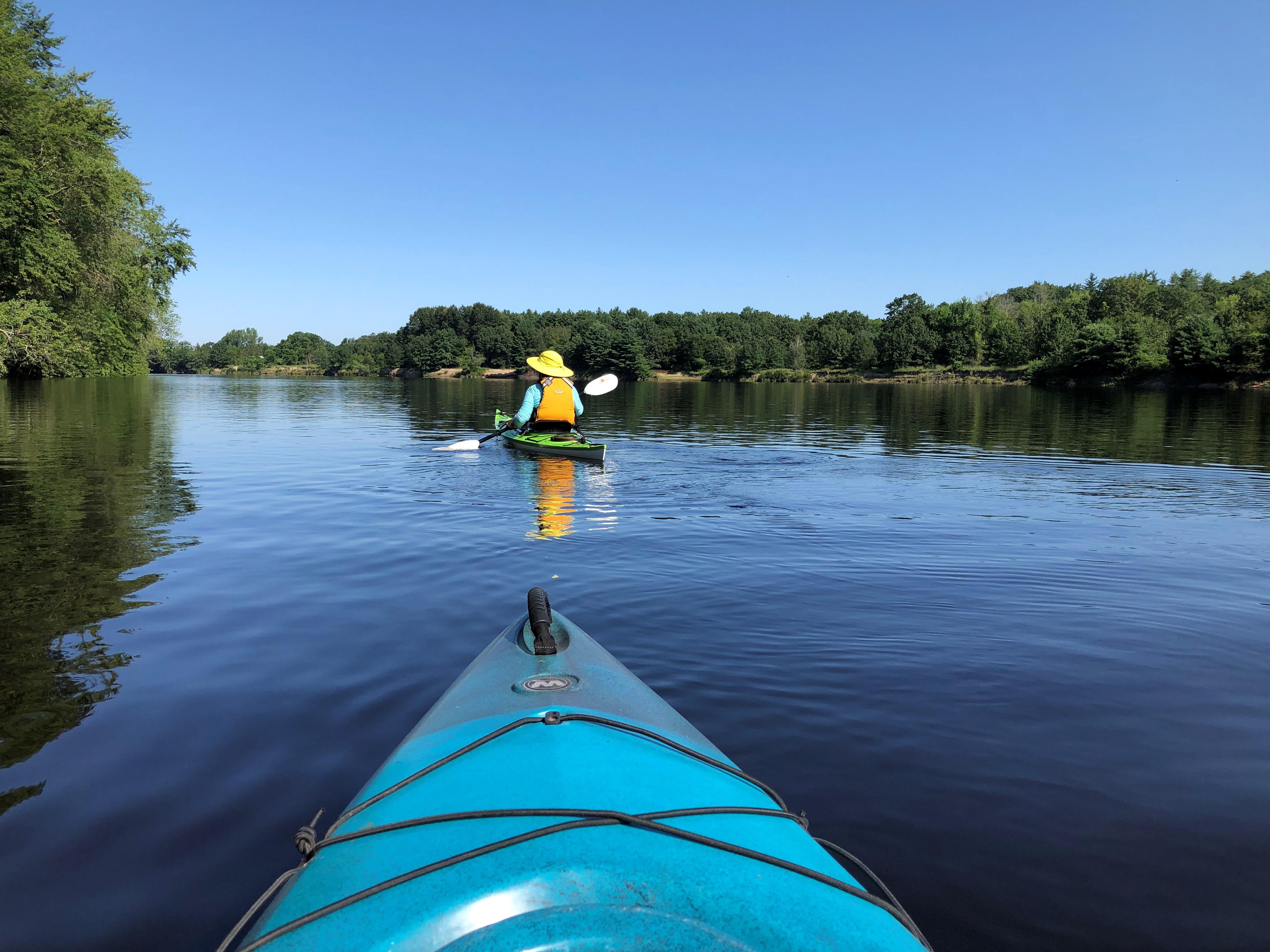 The front of a kayak in the river with another kayaker ahead.
