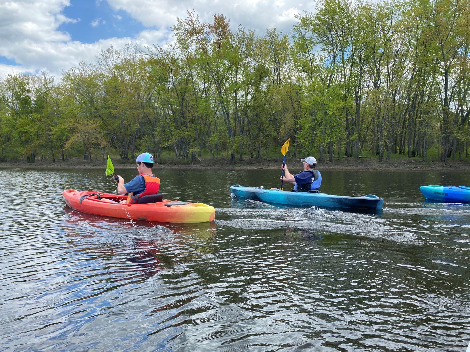 A father and son, both in lifejackets, kayak together on the Merrimack River.