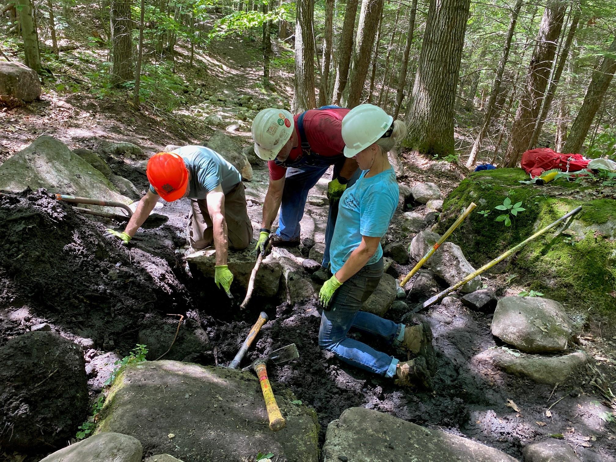 A group huddles around a muddy hole.