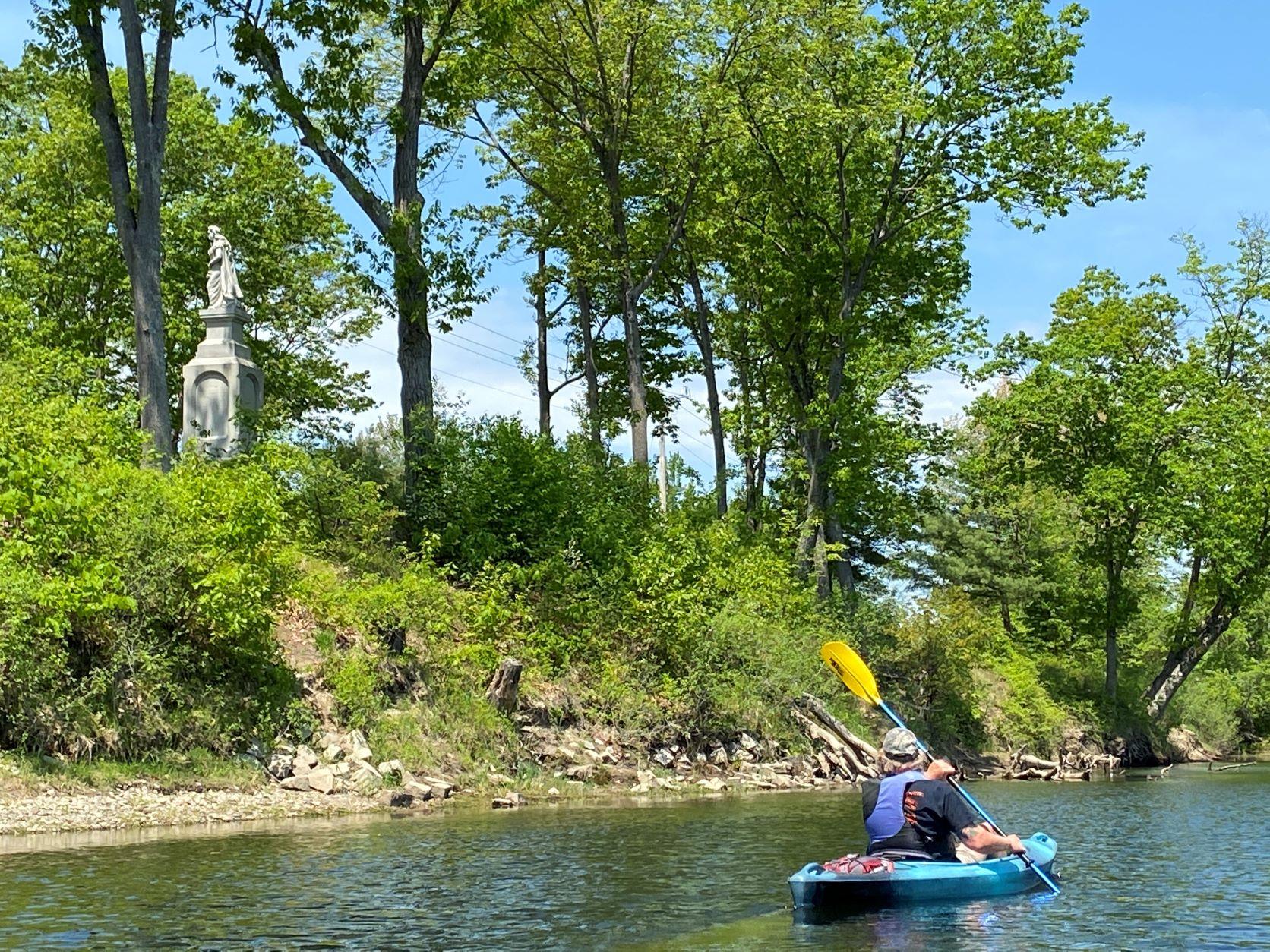 Dave Anderson paddles by a statue and looks up from the river.