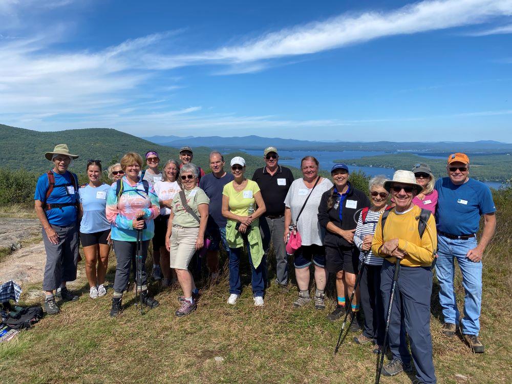 colorful hikers pose at open summit for portrait with scenic mountains and lake background
